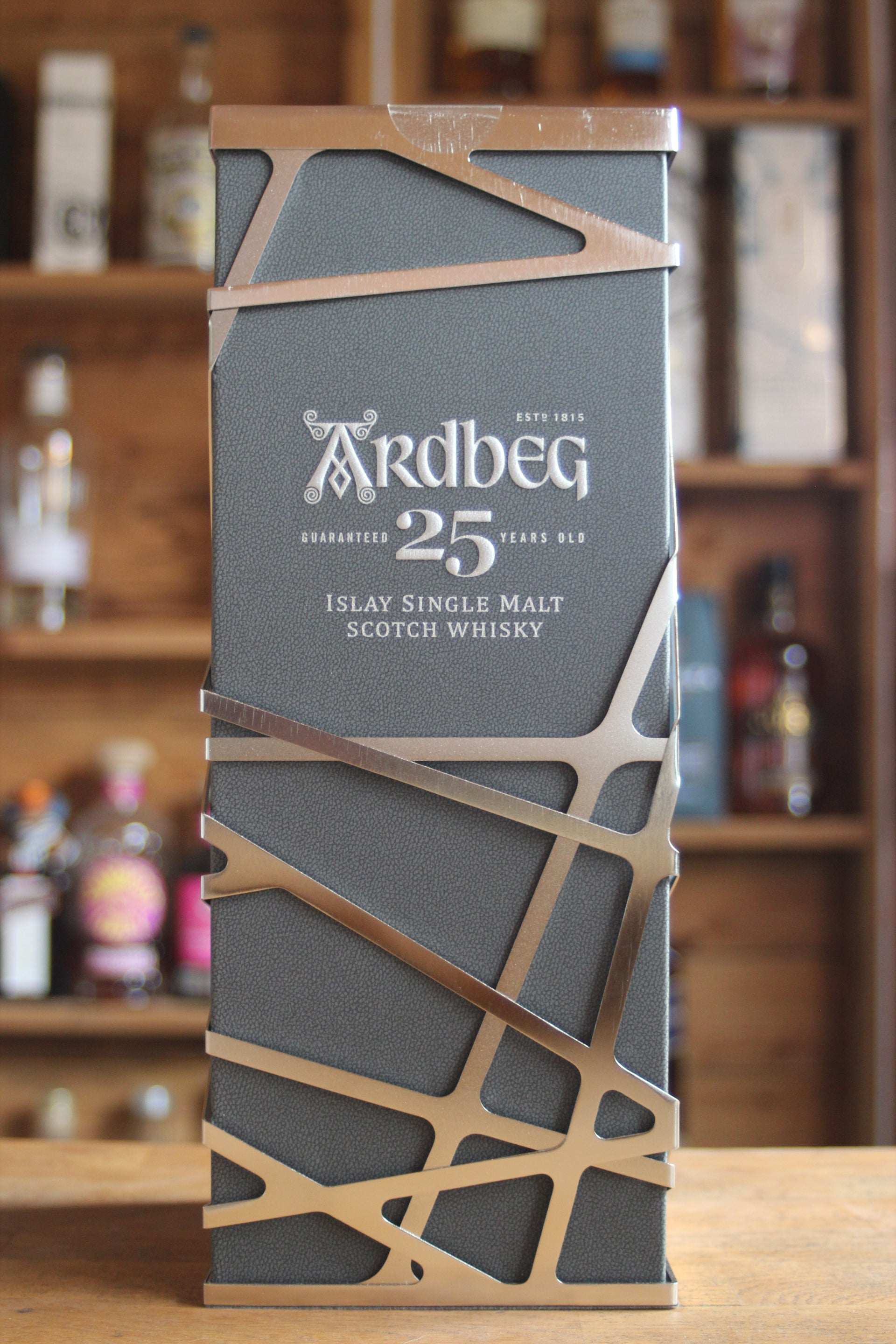 A bottle of Ardbeg 25-year-old whisky with a decorative label against a blurred bar background.